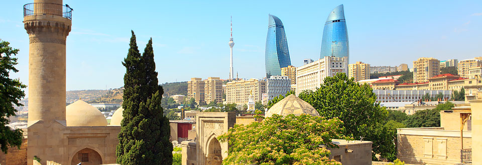 Billedet viser en by med moderne bygninger og historisk arkitektur under en klar blå himmel.