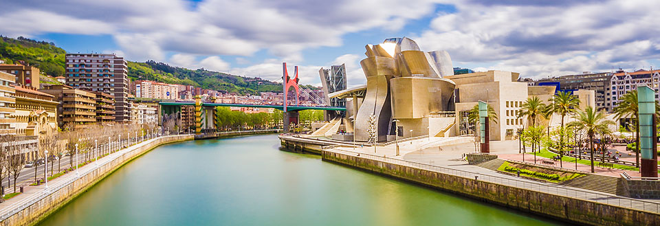 Moderne arkitektur dominerer dette billede af et berømt museum ved en flod, omkranset af grønne træer og bygninger.