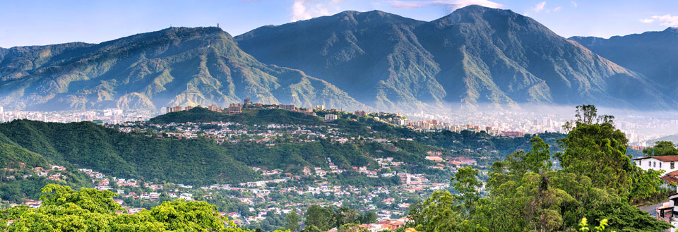 Panoramabillede af en by omgivet af frodige grønne bjerge og klar himmel.