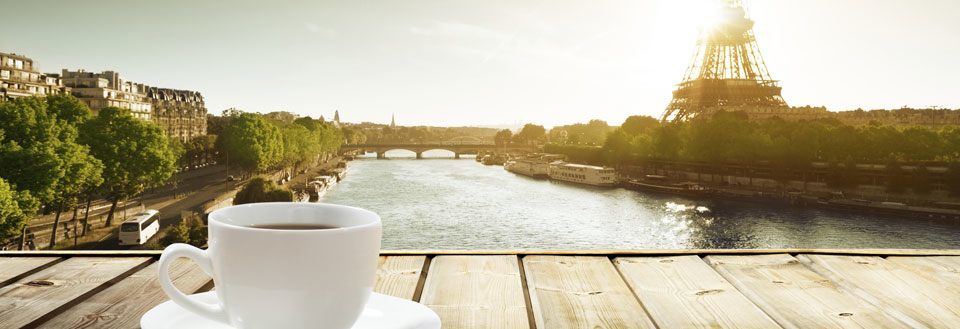 En hvid kaffekop på et træbord med udsigt over Seinen og Eiffeltårnet i Paris.