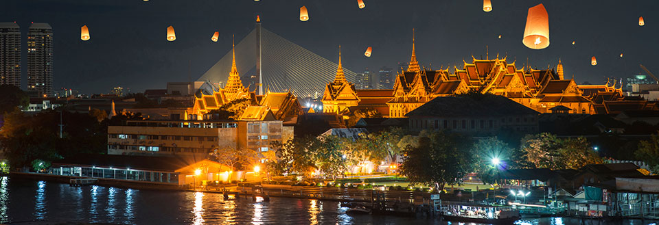 Billedet viser en flod ved nat med traditionelle lanterner svævende i luften over et thailandsk tempel.