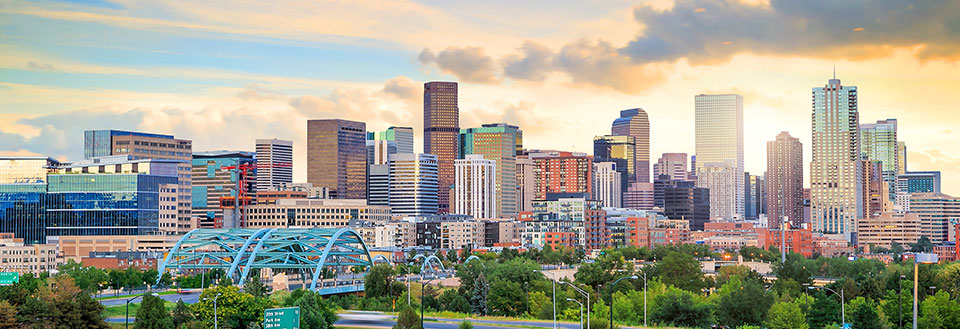Denvers Skyline med moderne bygninger og en blå bro foran. Skyerne danner en dramatisk baggrund.