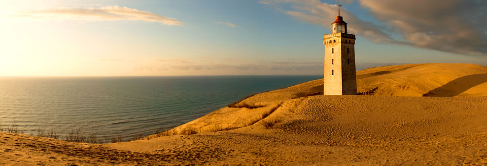 Rubjerg Knude fyr ved kysten omgivet af sandklitter under en gylden solnedgang.