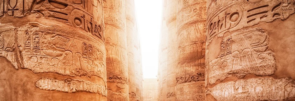 Billede viser gamle hieroglyffer på søjlerne i et egyptisk tempel badet i gyldent lys.
