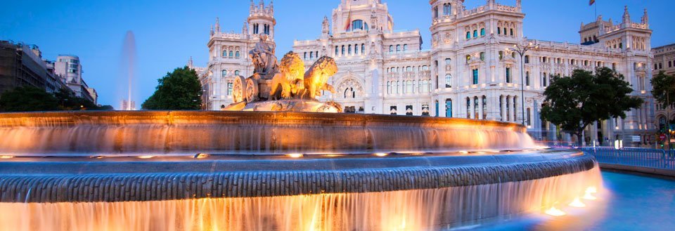 Billedet viser en majestætisk fontæne foran en imponerende bygning i skumringen.
