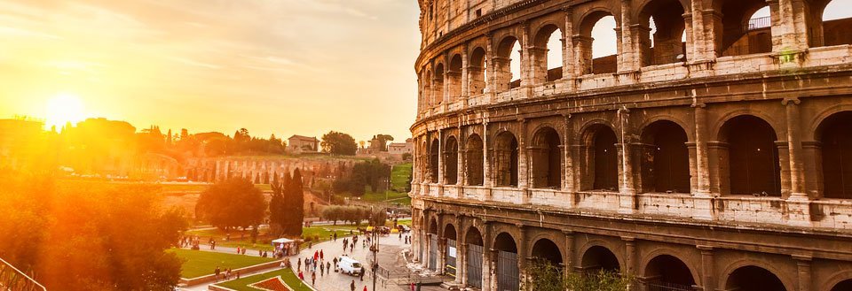 Colosseum i Rom under en solnedgang med besøgende, der går i nærheden.