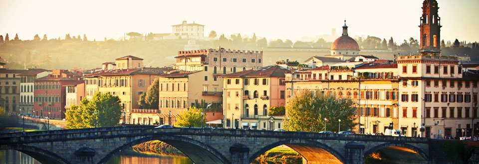 Solnedgang over Arnofloden i Firenze med en stenbro i forgrunden og historiske bygninger i baggrunden.