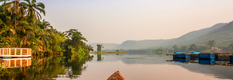 Rolig flod omgivet af tropisk vegetation i tåget morgenlys, med flydende strukturer og en kano i forgrunden.