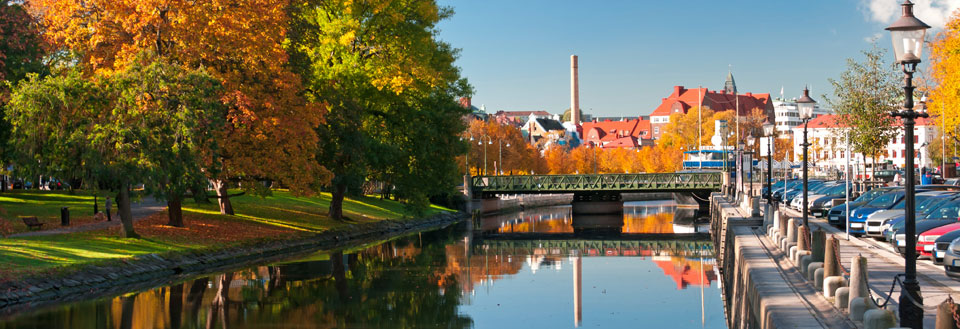 Fredelig flod, som løber igennem en by med farverige træer i efteråret og en klar blå himmel.