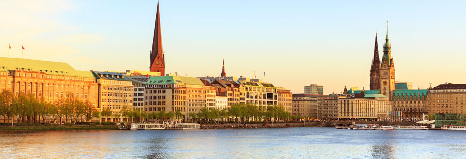 Panoramaudsigt over Hamborg med en travl søbred, med moderne bygninger og historiske kirkespir.