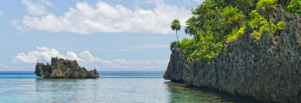 Klippeformationer og grøn bevoksning ved en tropisk strand med klart, blåt vand.