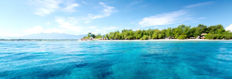 Panoramaudsigt over tropisk strand med krystalklart blåt vand og bjergrække i baggrunden.
