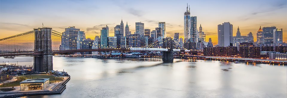 Panoramaudsigt over New York ved solnedgang med en berømt bro og oplyste skyskrabere.