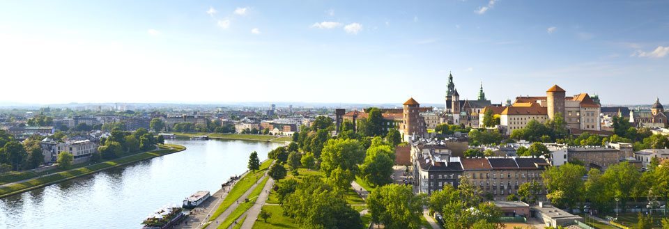 Panoramaudsigt over en europæisk by med historiske bygninger og et slot ved en flod omgivet af grønne områder.