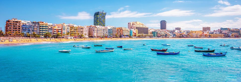 Strandlinje på Gran Canaria med farverige bygninger og flere både forankret i det blå hav.