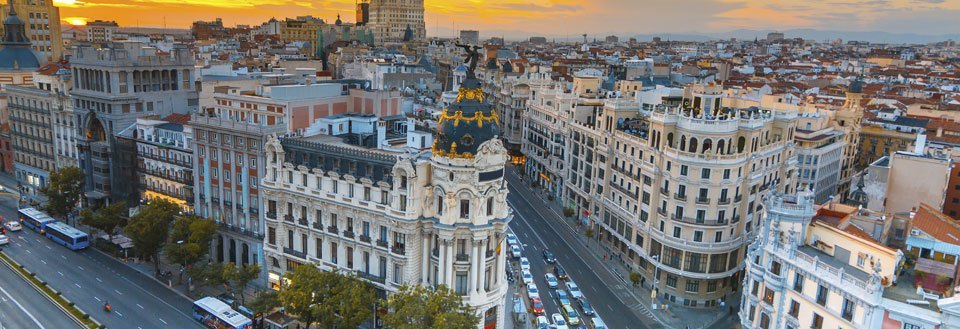 Solnedgang over Madrid med historiske bygninger og trafikerede veje.