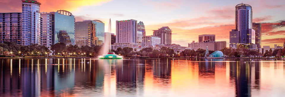 Orlandos silhuet ved solnedgang med bygninger, der spejler sig i en rolig vandflade.