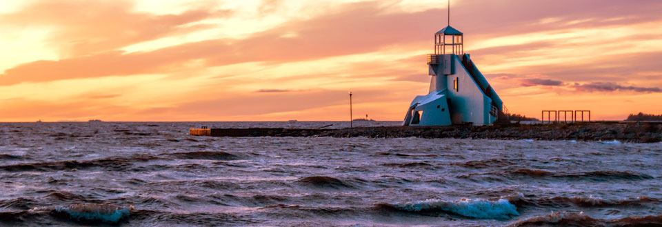 Et fyrtårn ved havet under en farverig solnedgang med oprørte bølger.