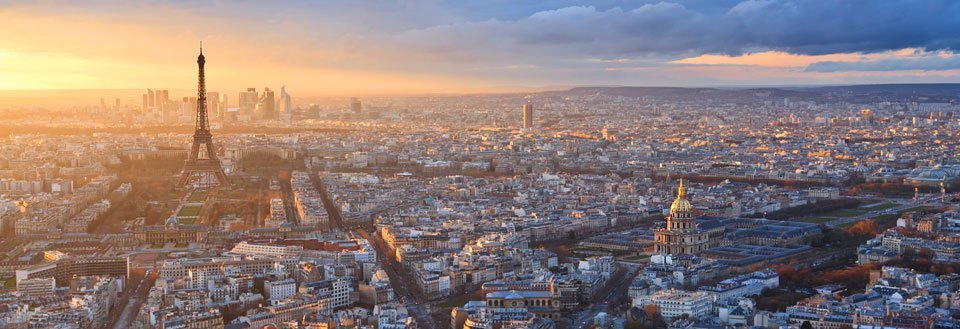 Panoramaudsigt over Paris ved solnedgang med Eiffeltårnet og byens tætte bebyggelse.