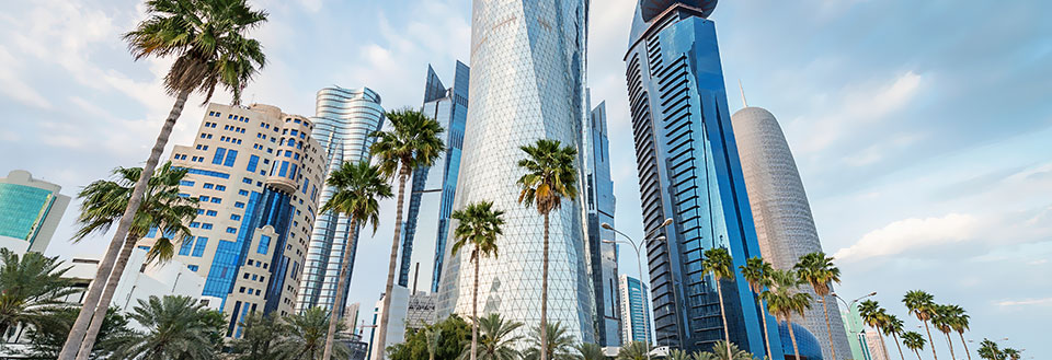 Moderne skyskrabere flankeret af palmetræer under en klar blå himmel.