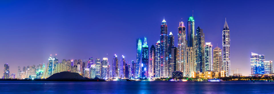 Dubais skyline om natten med oplyste skyskrabere og roligt vand foran.