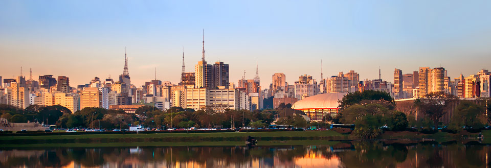 Sao Paulos skyline ved solnedgang med højhuse reflekteret i en sø.