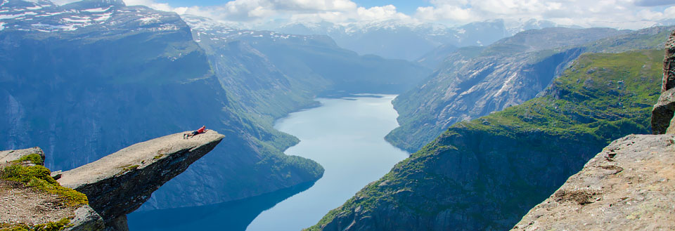 En person ligger på kanten af Trolltunga med benene udstrakte over en majestætisk fjord.