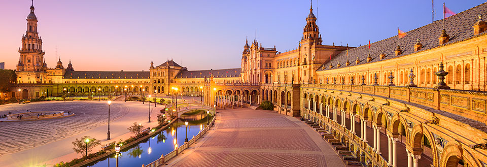 Plaza de España i Sevilla ved skumring med belysning, refleksion i vand og imponerende arkitektur.