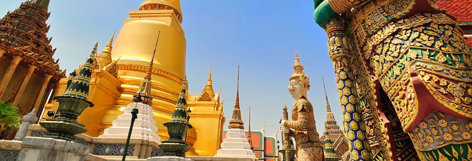 Grand Palace i Bangkok med gyldne stupas, farverige mosaikker og traditionelle statuer under en klar blå himmel.