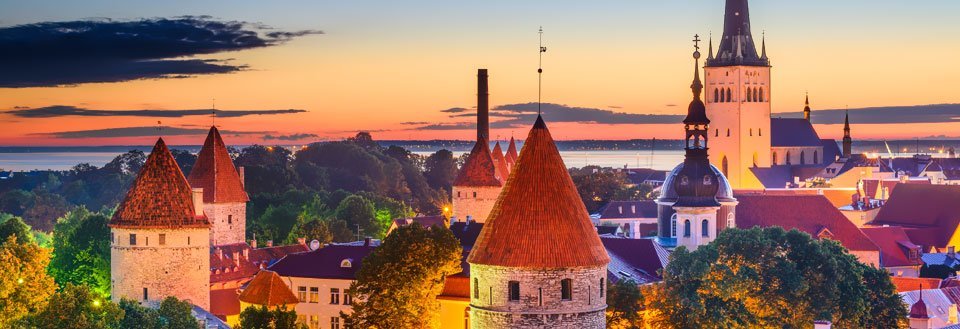 Tallinn ved solnedgang med tårne og kirkespir, mod en himmel i farverigt skær.