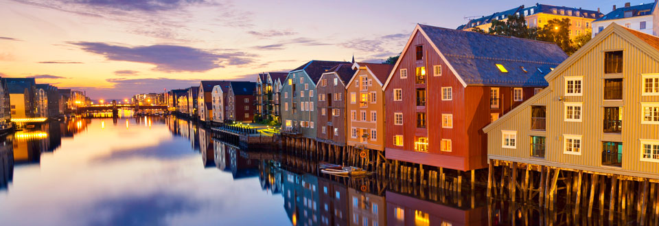 Farverige træhuse spejler sig i vandet ved skumring i Trondheim.
