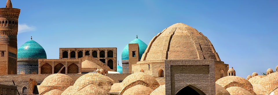 Ældgamle kupler og minareter under en klar himmel, hvilket tyder på, det er et historisk islamsk anlæg.