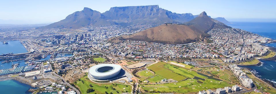 Panoramaudsigt over Cape Town med et stadion, havnefaciliteter og et fjeld i baggrunden.