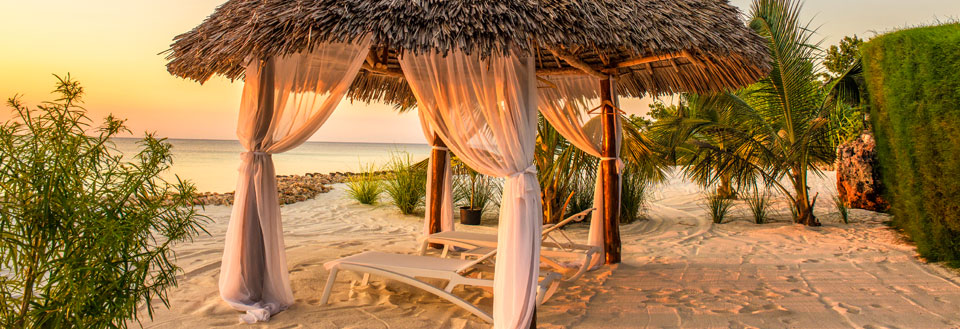 Romantisk strandhytte med hvide gardiner ved solnedgang, klar til afslapning.