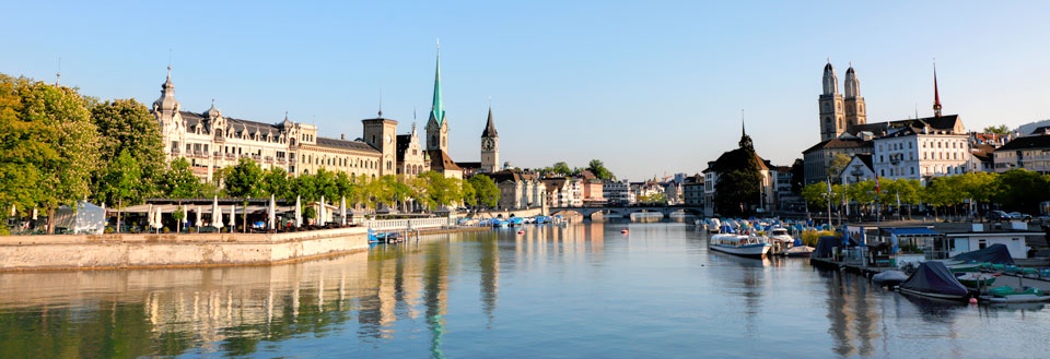 En panoramaudsigt over en fredelig flod i en europæisk by med både, bygninger og kirker.