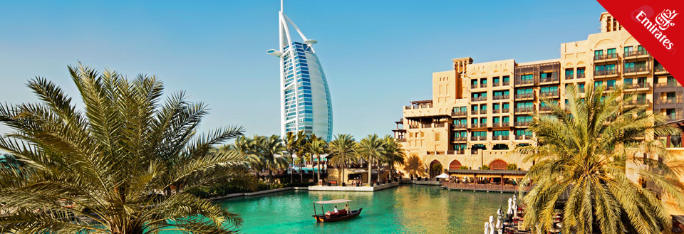 Det ikoniske Burj Al Arab hotel i Dubai, med en traditionel båd på vandet og palmer i forgrunden.