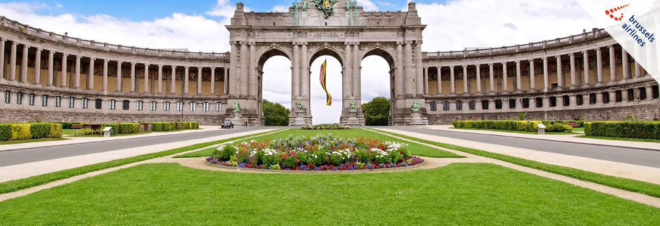 Triumfbuen i Bruxelles med grønne plæner og farverige blomster i forgrunden.