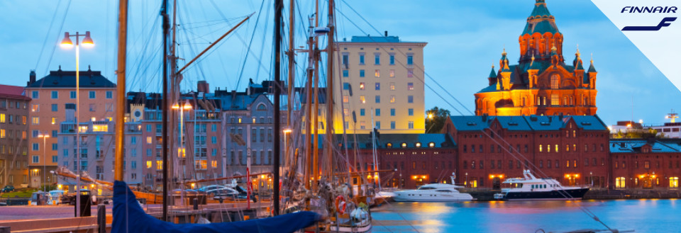 Aftenbilledet viser en havn med sejlbåde, farverige bygninger og en oplyst katedral i baggrunden.