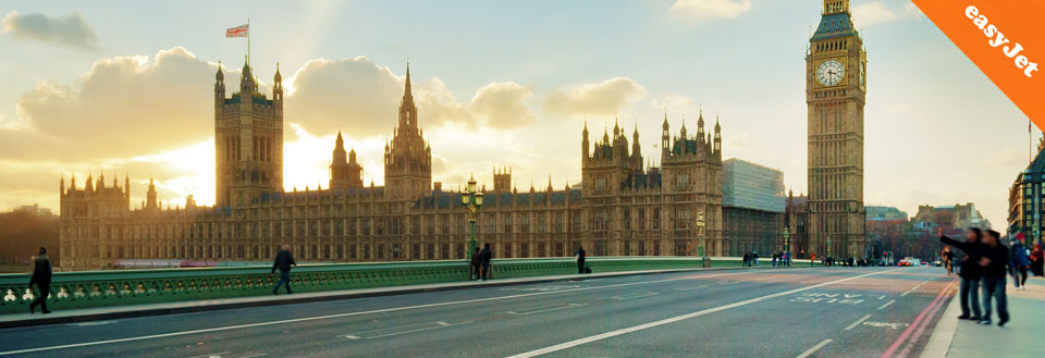 Folk krydser broen med solnedgangslys over Westminster Palace og Big Ben i London. 