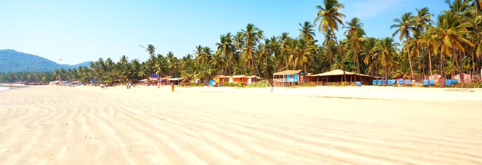 Solrig strand med gyldent sand, palmer og farverige hytter.  