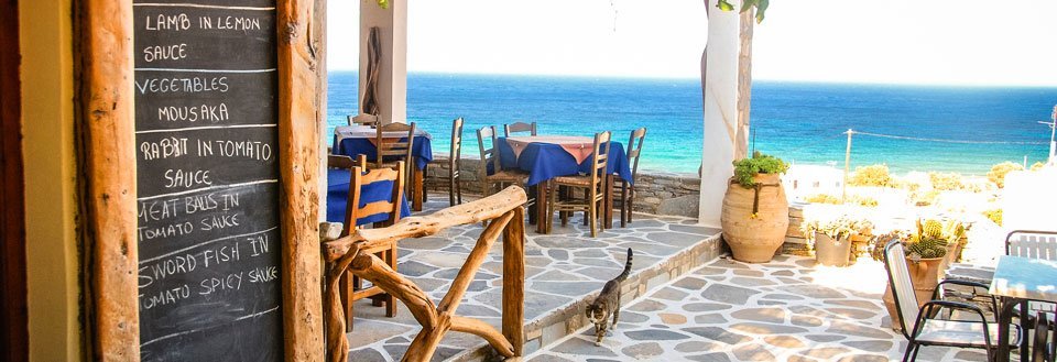 Hyggelig terrasse ved havet med menutavle samt bord og stole.