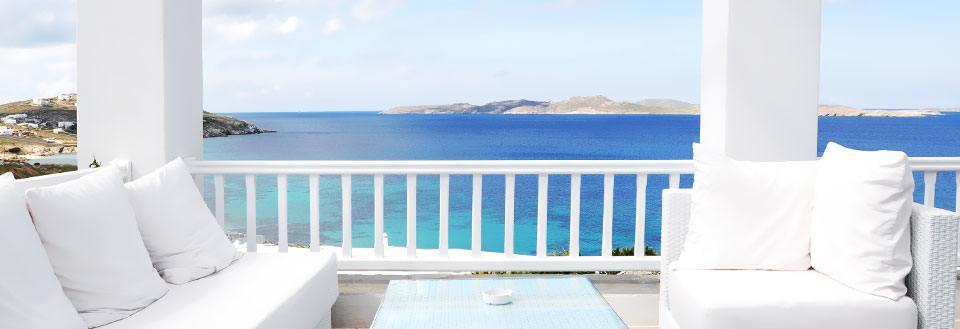 En hvid balkon med behagelige sofaer og storslået udsigt over det azurblå hav og en kystlinje.