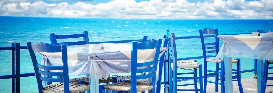 Et hyggeligt udendørs spiseområde med blå stole foran en smuk havudsigt.