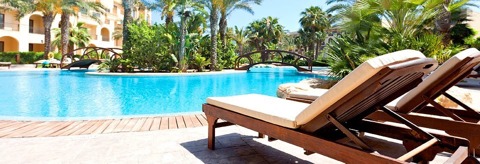 Et luksuriøst poolområde ved et ferieresort med liggestole, palmer og en klar blå swimmingpool.