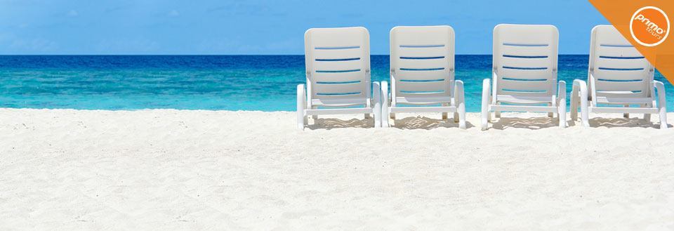Fire hvide liggestole står på en solrig sandstrand med en klar blå himmel og turkis hav i baggrunden.