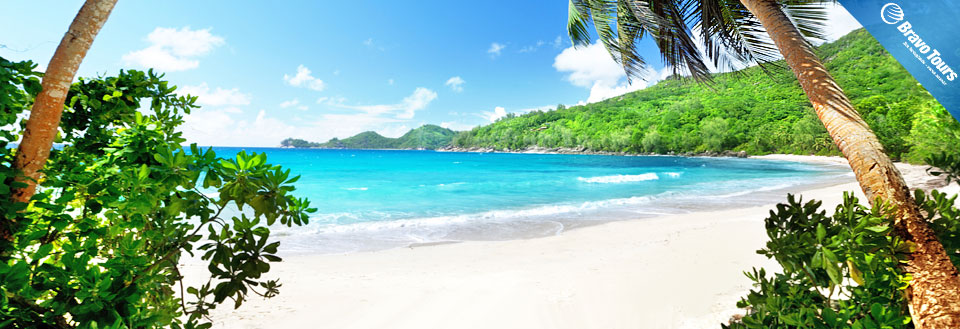 Et idyllisk tropisk strandlandskab med krystalklart blåt vand, frodige grønne træer og en klar blå himmel.