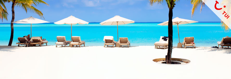 Hvid sandstrand med parasoller og liggestole foran turkis hav under en klar blå himmel.