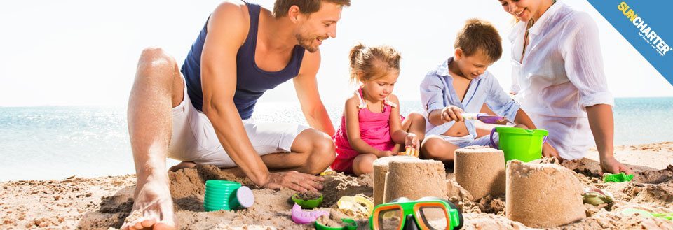 En familie nyder solen på stranden mens de bygger sandslotte sammen.