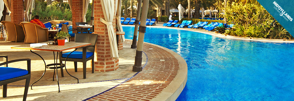 Et luksuriøst poolområde med liggestole og en terrasse med borde og stole under parasoller.