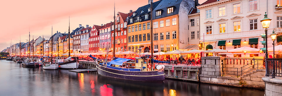 Farverige bygninger og restauranter langs kanalen i København ved solnedgang.